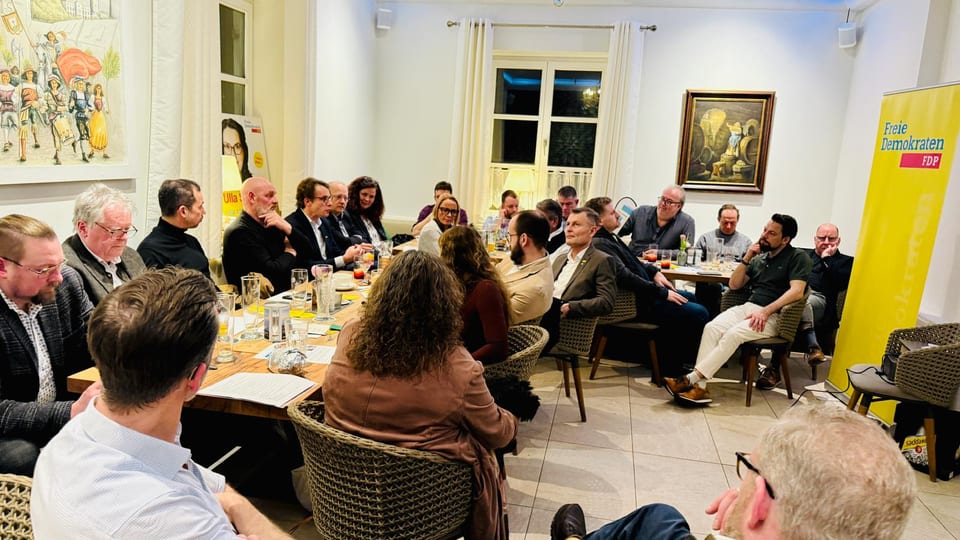 Voll besetzter Raum beim Liberalen Impulsdialog, Gäste sitzen an Tischen um die Redner, rechts ein Banner der Freien Demokraten
